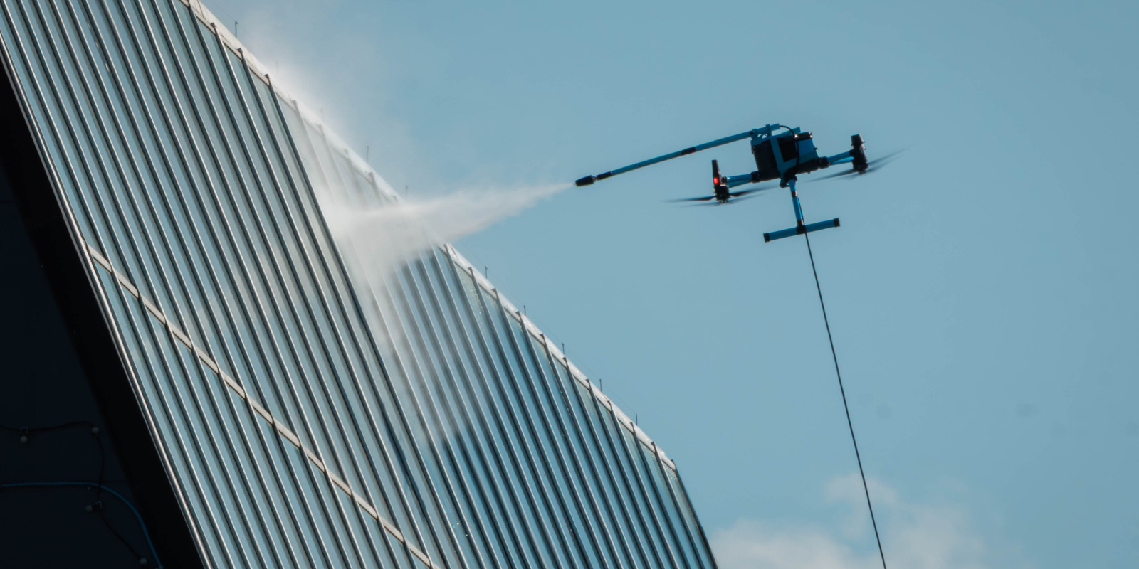 Unmanned aerial drone applying low pressure soft wash treatments to commercial building siding